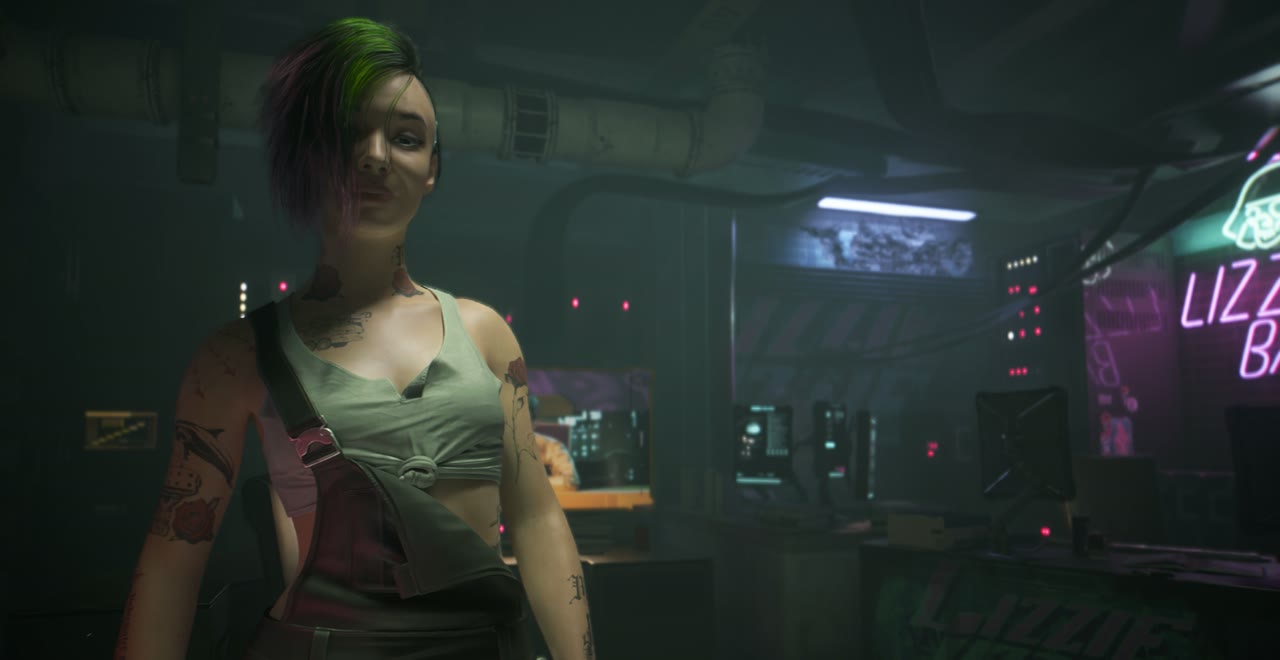 緑とピンクの髪にタトゥーのジュディ・アルヴァレスが、奥に「LIZZIE'S BAR」のネオンが見える部屋に立っている場面